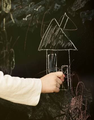 Kind kritzelt mit Kreide auf einer Tafel herum Macro shot of kids hand draws house on blackboard BLWS237816