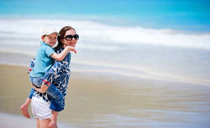 junge Mutter traegt ihren kleinen Sohn huckepack am Strand young mother carrying piggyback her young son BLWS269838