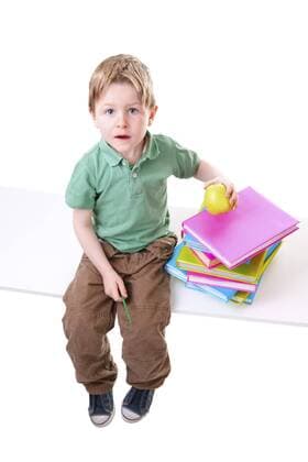 kleiner Junge sitzt auf einer Bank mit einem Stapel Buecher und einem Apfel Little boy with books with a pile of books and an apple BLWS238341
