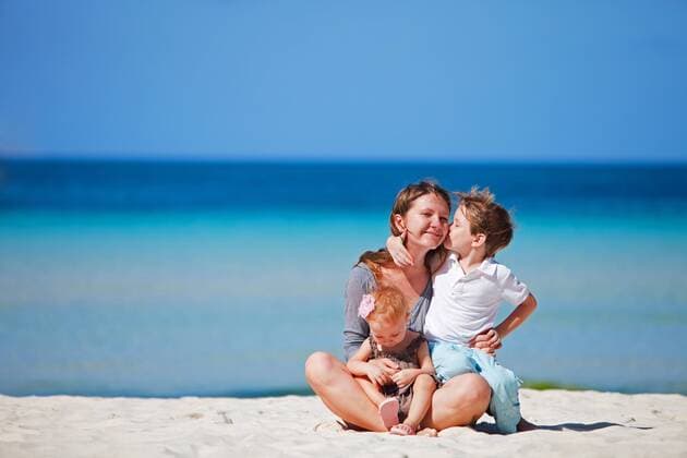 junge Frau sitzt mit ihren zwei kleinen Kindern am Sandstrand young woman sitting with her two little children on sandy beach BLWS269824