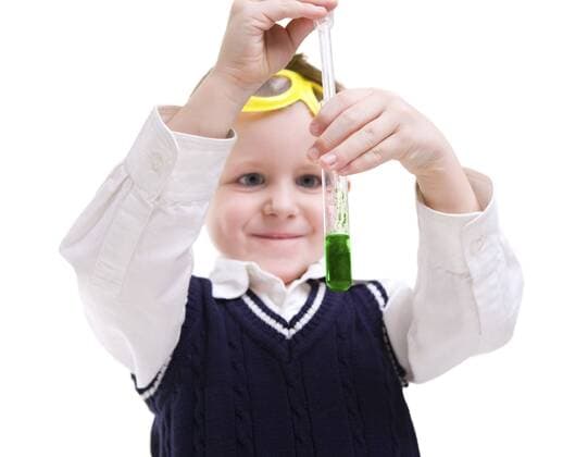 kleiner Forscher fuellt gruene Fluessigkeit in eine Reagenzglas Early education. Young boy performing chemistry experiments BLWS237752