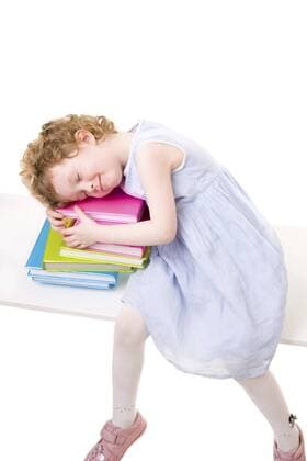 kleines Kind sitzt auf einer Bank und ist auf einem Stapel Buechern eingeschlafen Little girl with books BLWS237826