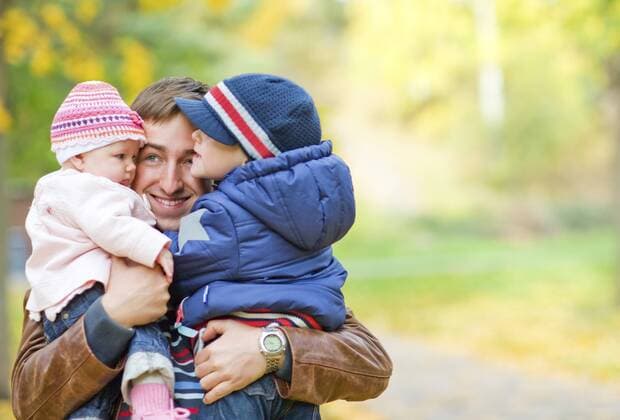 junger Vater mit seinen beiden Kindern auf dem Arm auf einem Spaziergang an einem Herbsttag Young father with two kids enjoying beautiful autumn day BLWS237843