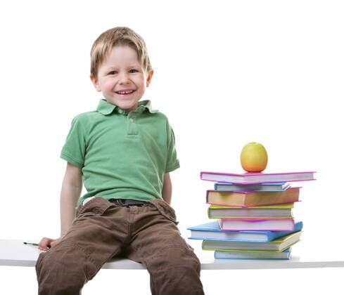 kleiner Junge sitzt auf einer Bank mit einem Stapel Buecher und einem Apfel Little boy with books with a pile of books and an apple BLWS238335