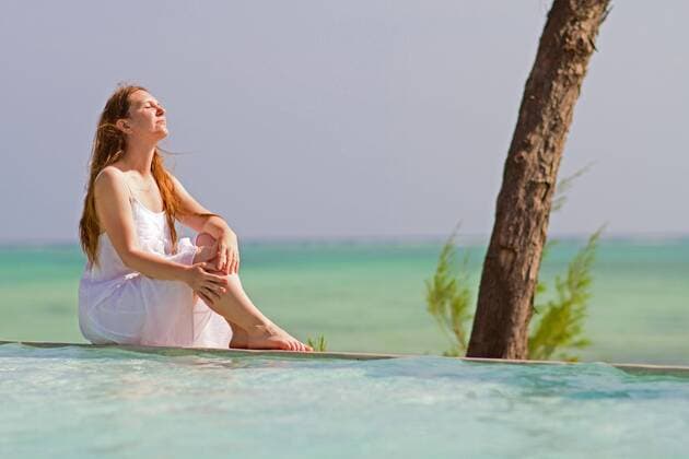 eine schoene Frau im Strandkleid sitzt am Rand eines Swimmingpools eines tropischen Reiseziel a beautiful woman sitting at the pool edge near tropical beach BLWS269799