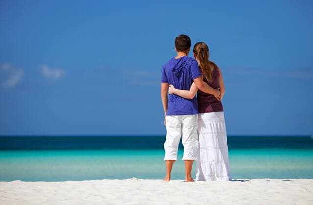 junges Paar steht am tropischen Sandstrand, umarmt sich und blickt auf das Meer young couple embracing on tropical beach and looking to the sea BLWS269829