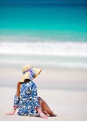 eine Frau mit Sonnenhut sitzt am Sandstrand, Rueckansicht woman with sun hat sitting on sandy beach, rear view BLWS269836