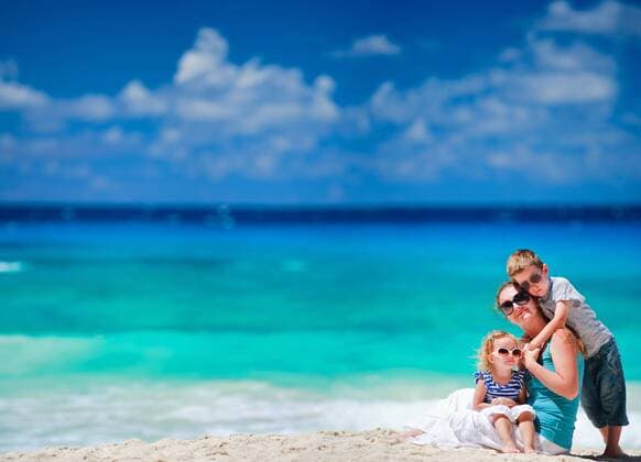 junge Mutter sitzt mit ihrer kleinen Tochter und ihrem Sohn am Sandstrand young mother and her daughter sitting on sandy beach, her son embracing her BLWS270936