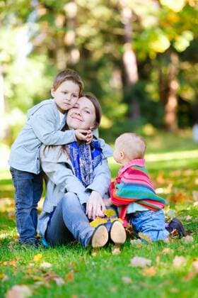 eine junge Mutter sitzt mit ihren zwei Kindern auf dem Rasen an einem sonnigen Herbsttag a young mother sitting with her two children into meadow on a sunny autmn day BLWS272218