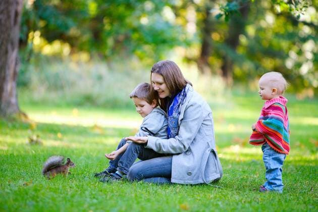 Mutter mit zwei kleinen Kindern fuettert ein Eichhoernchen im Park mother and her two children feeding a red squirrel BLWS272219