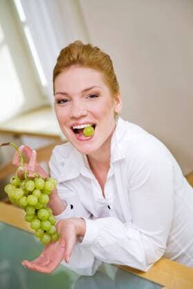 Woman eating grapes, sitting next to the table.  1272429