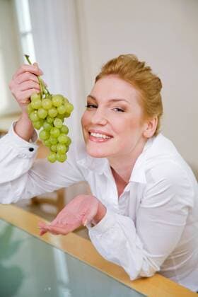Woman eating grapes, sitting next to the table.  1272431