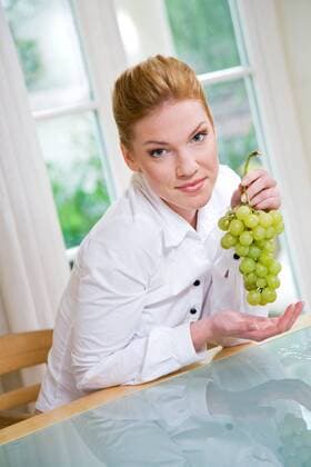 Woman eating grapes, sitting next to the table.  1272433