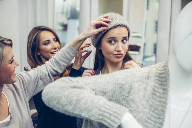 Young woman putting on woolly hat in a boutique assisted by two women model released Symbolfoto property released  CHAF001347