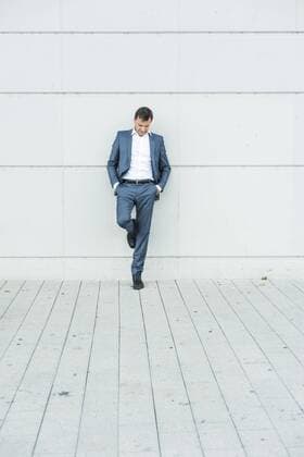 Businessman leaning on wall with hands in pockets model released Symbolfoto  UUF005226