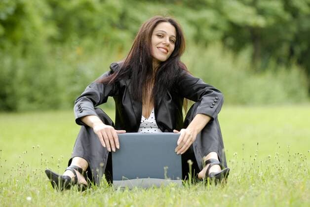 junge Frau sitzt mit Laptop auf einer Wiese young woman sitting in a meadow with a laptop BLWS243420