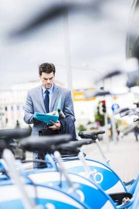 Businessman standing behind rental bikes looking at documents model released Symbolfoto  UUF005367