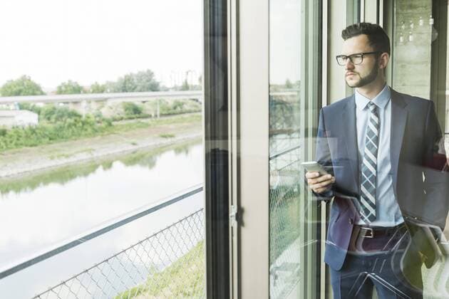 Young businessman with cell phone looking out of window model released Symbolfoto property released  UUF005410