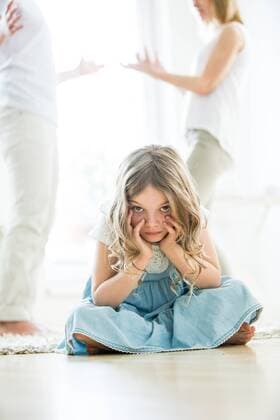 Little girl sitting cross-legged on floor, parents arguing in background model released Symbolfoto property released  WESTF021531