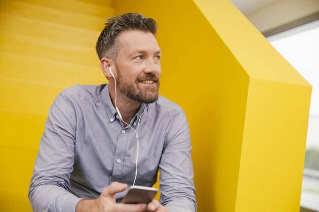 Portrait of smiling mature man hearing music with smartphone and earphones sitting on yellow stairs model released Symbolfoto property released  MFF002126
