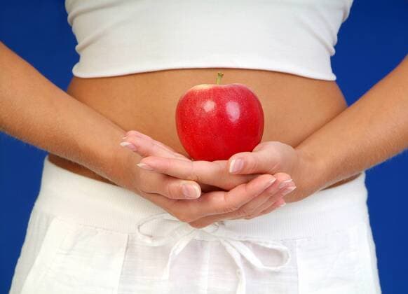Frau haelt einen roten Apfel vor den Bauch woman holding a red apple in front of her belly BLWS150622