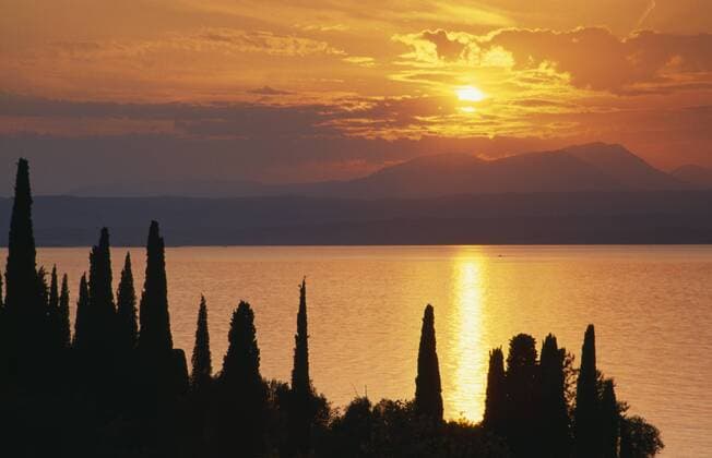 ITALY Lombardy Lake Garda Sunset over Lake Garda from Punta San Vigilio with trees silhouetted against water reflecting orange sky. Copyright: xEyexUbiquitous 904_14_20088320