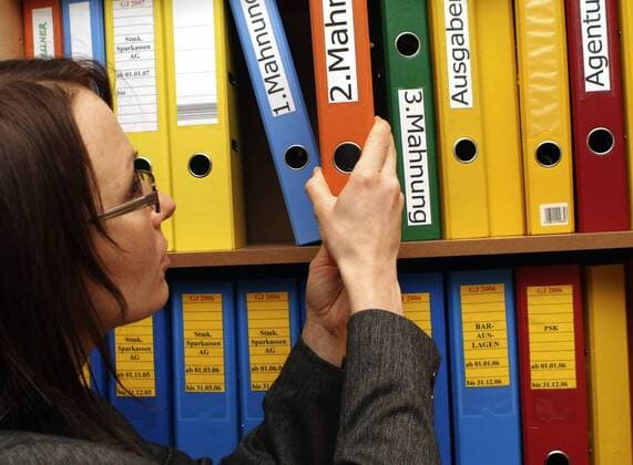 Bueroangestellte nimmt Aktenordner aus Regal woman clerk takes files from filing cabinet BLWS162146