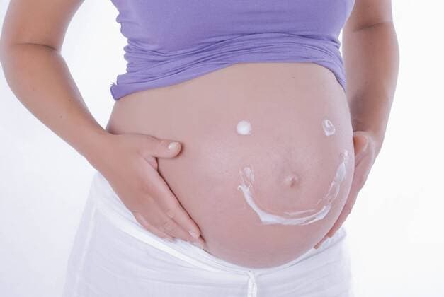 Lachendes Cremegesicht auf dem Babybauch einer jungen Frau smiling face on baby belly BLWS241596