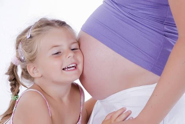 Maedchen horcht am Babybauch der Mutter girl touches baby belly of mother BLWS241592