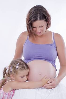 Maedchen horcht am Babybauch der Mutter girl touches baby belly of mother BLWS241593