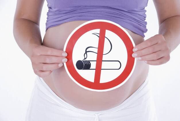 schwangere Frau haelt Rauchverbotsschild vor Babybauch ban of smoking when pregnant BLWS241599
