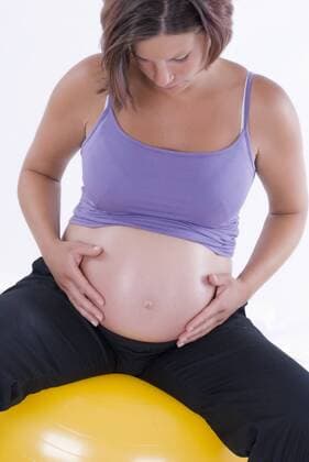 schwangere Frau sitzt auf Gymnastikball und haelt sich den Bauch pregnant woman on fit ball BLWS241600