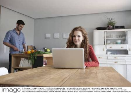 Woman at home using laptop with man in background cutting vegetables model released Symbolfoto property released  RBF003543