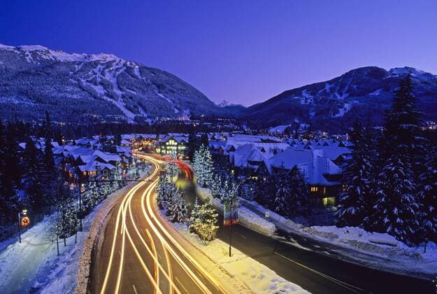 Lorimer Road is lit with Christmas lights in Whistler, BC. Whistler Mountain and Blackcomb Mountain rise in the distance.  acp79539 LeannaxRathkelly