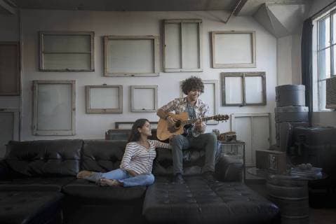 Loft decor. A wall hung with pictures in frames, reversed to show the backs. A man playing a guitar and a woman sitting on a sofa. Loft decor. A wall hung with pictures in frames, reversed to show the backs. A man playing a guitar and a woman sitting on a sofa.  18900