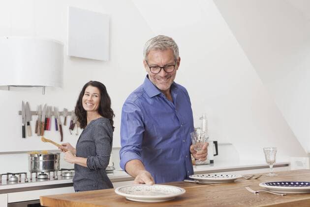 Mature couple cooking in kitchen with woman cooking and man laying the table model released Symbolfoto property released  RBF003746