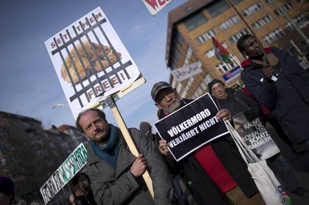 Gedenkmarsch Kolonialgeschichte DEU, Deutschland, Germany, Berlin, 27.02.2016 Demonstranten mit Plakat Voelkermord verjaehrt nicht und Set them Free beim 10. Gedenkmarsch zur Erinnerung an die afrikanischen Opfer von Versklavung, Kolonialismus und rassistischer Gewalt vom Komitee fuer ein afrikanisches Denkmal in Berlin und afrikanischer Vereine in Berlin. Dieser Gedenkmarsch wurde ins Leben gerufen, um der Forderung nach Anerkennung der Verbrechen gegen Schwarze Menschen und Menschen afrikanischer Herkunft Nachdruck zu verleihen. Anlass ist die Berliner Afrika-Konferenz von 1884 - 1885, auf der Afrika vor 130 Jahren unter den europaeischen Kolonialmaechten aufgeteilt wurde. Mehr als 30 Millionen Afrikanerinnen und Afrikaner wurden Opfer von Versklavung und kolonialen Verbrechen gegen die Menschlichkeit. Die von Deutschland an den Herero und Nama begangenen Voelkermorde in Namibia und di