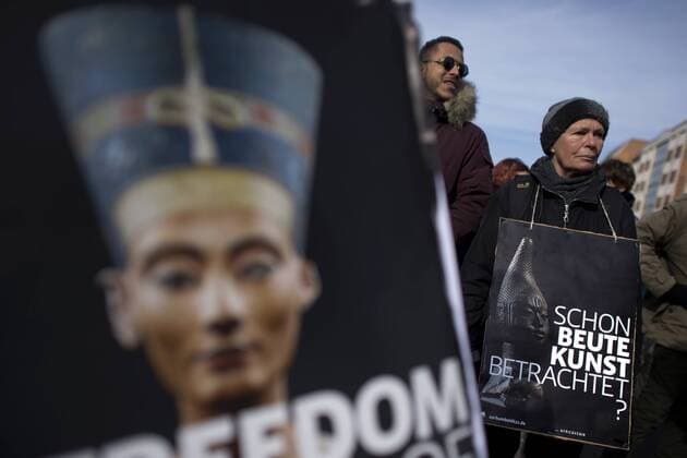 Gedenkmarsch Kolonialgeschichte DEU, Deutschland, Germany, Berlin, 27.02.2016 Demonstrant mit Plakat Freedom of Movement Schon Beutekunst betrachtet und Foto der Nofretete gegen die Kolobialgeschichte und die Aneigung afrikanischer Kulturgueter durch deutsche Museen und dem Humboldt Forum beim 10. Gedenkmarsch zur Erinnerung an die afrikanischen Opfer von Versklavung, Kolonialismus und rassistischer Gewalt vom Komitee fuer ein afrikanisches Denkmal in Berlin und afrikanischer Vereine in Berlin. Dieser Gedenkmarsch wurde ins Leben gerufen, um der Forderung nach Anerkennung der Verbrechen gegen Schwarze Menschen und Menschen afrikanischer Herkunft Nachdruck zu verleihen. Anlass ist die Berliner Afrika-Konferenz von 1884 - 1885, auf der Afrika vor 130 Jahren unter den europaeischen Kolonialmaechten aufgeteilt wurde. Mehr als 30 Millionen Afrikanerinnen und Afrikaner wurden Opfer von Verskla