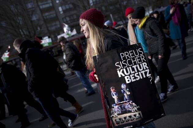 Gedenkmarsch Kolonialgeschichte DEU, Deutschland, Germany, Berlin, 27.02.2016 Demonstrant mit Plakat Preussischer Kulturbesitz gegen die Kolobialgeschichte und die Aneigung afrikanischer Kulturgueter durch deutsche Museen und dem Humboldt Forum beim 10. Gedenkmarsch zur Erinnerung an die afrikanischen Opfer von Versklavung, Kolonialismus und rassistischer Gewalt vom Komitee fuer ein afrikanisches Denkmal in Berlin und afrikanischer Vereine in Berlin. Dieser Gedenkmarsch wurde ins Leben gerufen, um der Forderung nach Anerkennung der Verbrechen gegen Schwarze Menschen und Menschen afrikanischer Herkunft Nachdruck zu verleihen. Anlass ist die Berliner Afrika-Konferenz von 1884 - 1885, auf der Afrika vor 130 Jahren unter den europaeischen Kolonialmaechten aufgeteilt wurde. Mehr als 30 Millionen Afrikanerinnen und Afrikaner wurden Opfer von Versklavung und kolonialen Verbrechen gegen die Mens