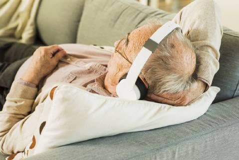 Senior man lying on the couch hearing music with headphones model released Symbolfoto property released  UUF006628