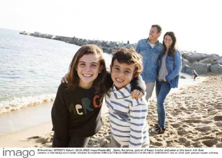 Spain, Barcelona, portrait of happy brother and sister on the beach with their parents in the background model released Symbolfoto  VABF000047