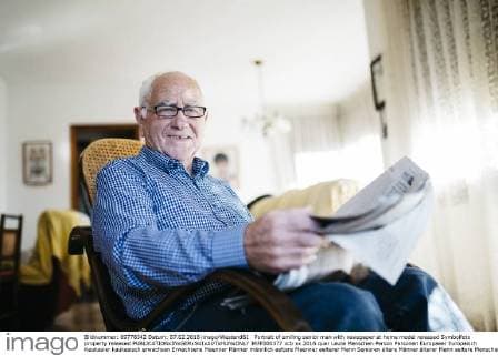 Portrait of smiling senior man with newspaper at home model released Symbolfoto property released  JRFF000377