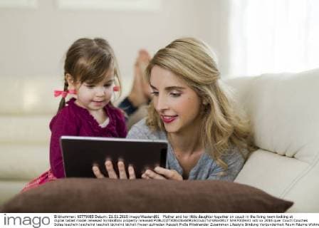 Mother and her little daughter together on couch in the living room looking at digital tablet model released Symbolfoto property released  SHKF000441