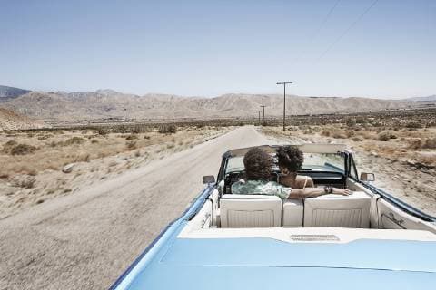 A young couple, man and woman in a pale blue convertible on the open road A young couple, man and woman in a pale blue convertible on the open road  19345