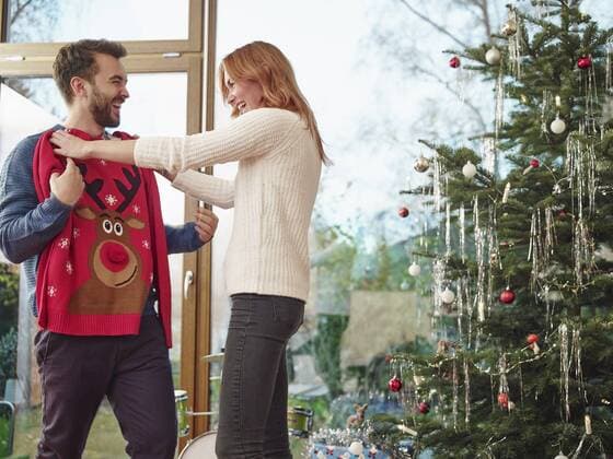 Couple standing in front of Christmas tree trying on Christmas jumper model released Symbolfoto property released  RHF001325