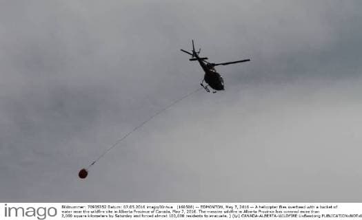 (160508) -- EDMONTON, May 7, 2016 -- A helicopter flies overhead with a bucket of water near the wildfire site in Alberta Province of Canada, May 7, 2016. The massive wildfire in Alberta Province has covered more than 2,000 square kilometers by Saturday and forced almost 100,000 residents to evacuate. ) (lyi) CANADA-ALBERTA-WILDFIRE LixBaodong 