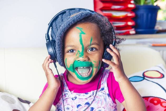 Portrait of happy little girl with painted face listening music with headphones model released Symbolfoto  YNF000017