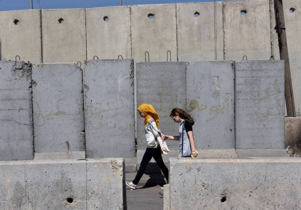 Palestinian youth walk between concrete barriers in front of the Israeli separation wall at the Qalandiya Checkpoint, West Bank, August 4, 2016. Palestinians in the northern West Bank must have permits to cross the Qalandiya Checkpoint to reach Jerusalem.  JER2016080418 DEBBIExHILL
