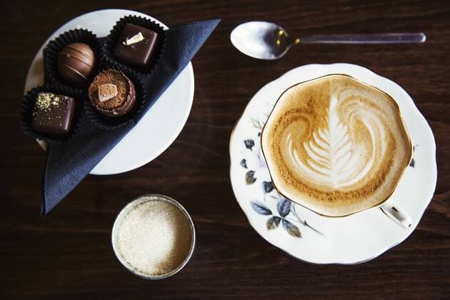 Assorted hand made chocolates on a plate. A cup of coffee with a pattern in the foam top. Assorted hand made chocolates on a plate. A cup of coffee with a pattern in the foam top.  23376