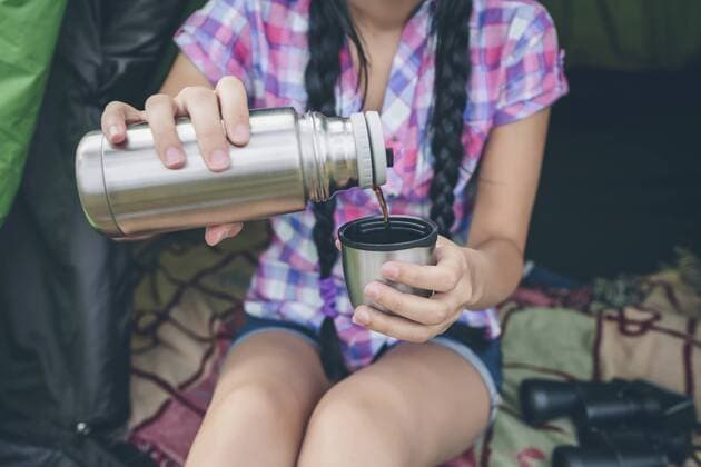 Young woman sitting in a tent pouring coffee from thermos flask into cup, partial view model released Symbolfoto  DAPF000261
